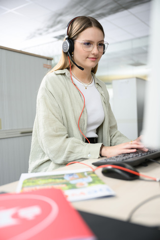 Eine Bürokauffrau telefoniert über ein Headset und sitzt am Computer.