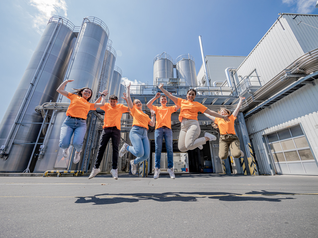 Azubis in orangenen Shirts springen vor Freude auf dem Werksgelände